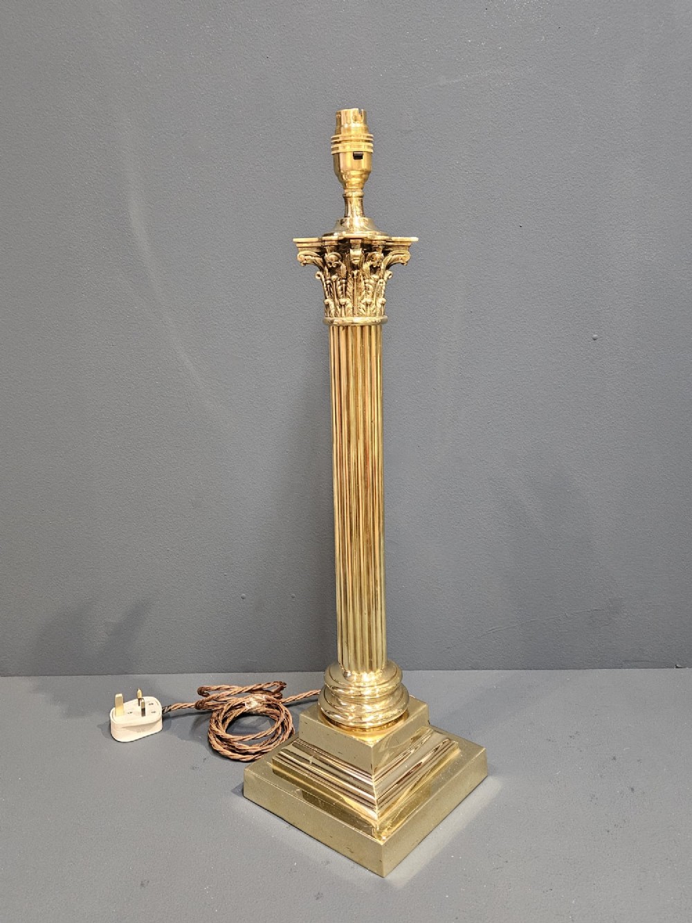 An Edwardian brass table lamp designed as a classical Corinthian column with a fluted shaft and stepped square base. View V