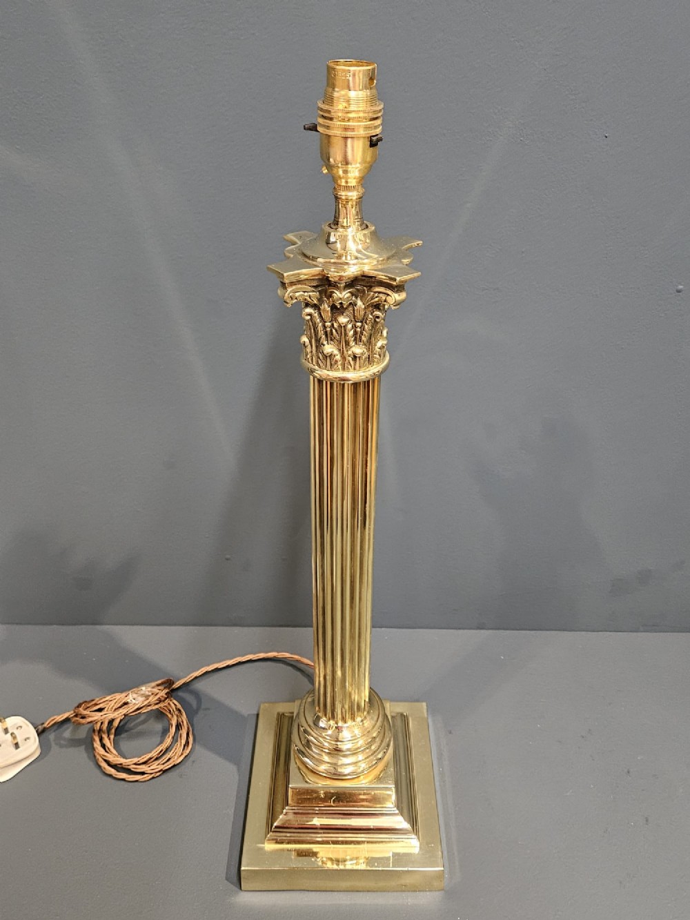An Edwardian brass table lamp designed as a classical Corinthian column with a fluted shaft and stepped square base. View VI