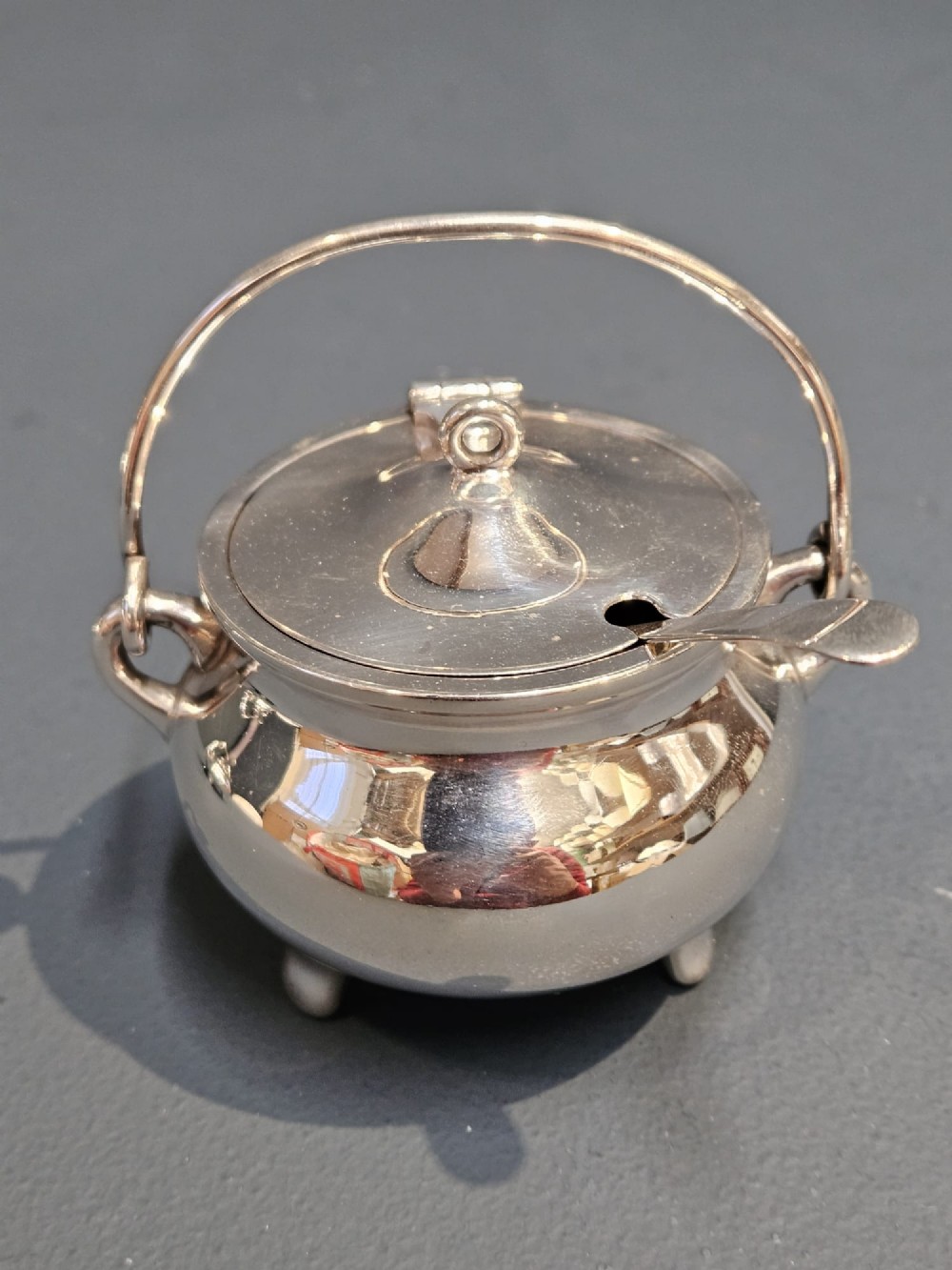 A pair of silver cauldron-shaped Edwardian mustard pots featuring overhead wire handles, hinged lids, and three small feet. View III