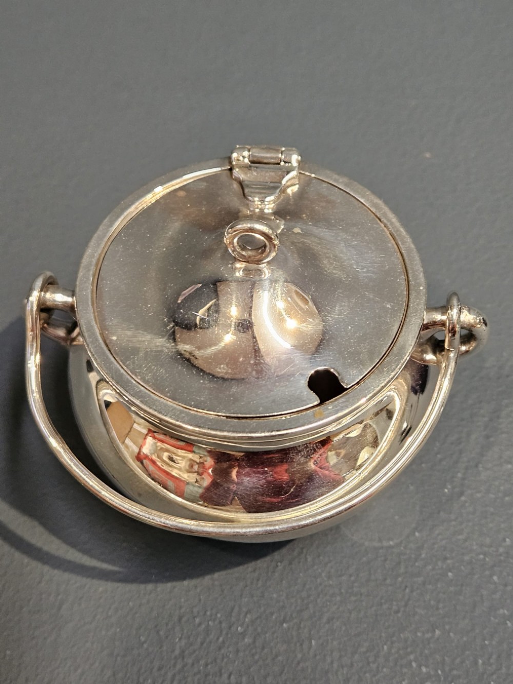 A pair of silver cauldron-shaped Edwardian mustard pots featuring overhead wire handles, hinged lids, and three small feet. View VI