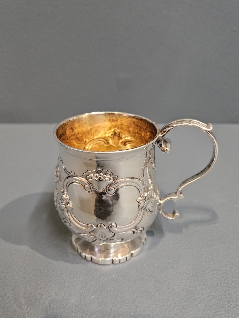 A William IV sterling silver mug featuring hand-chased floral cartouches, a scroll handle, a fluted foot, and a gilded interior. View II