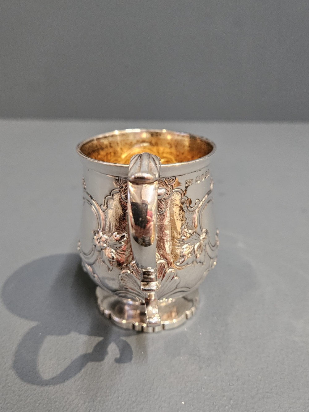 A William IV sterling silver mug featuring hand-chased floral cartouches, a scroll handle, a fluted foot, and a gilded interior. View III