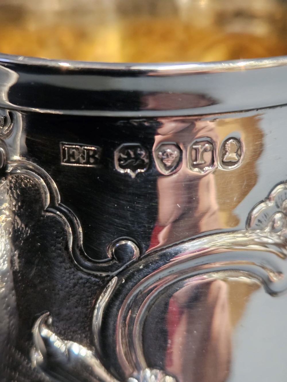 A William IV sterling silver mug featuring hand-chased floral cartouches, a scroll handle, a fluted foot, and a gilded interior. View IV
