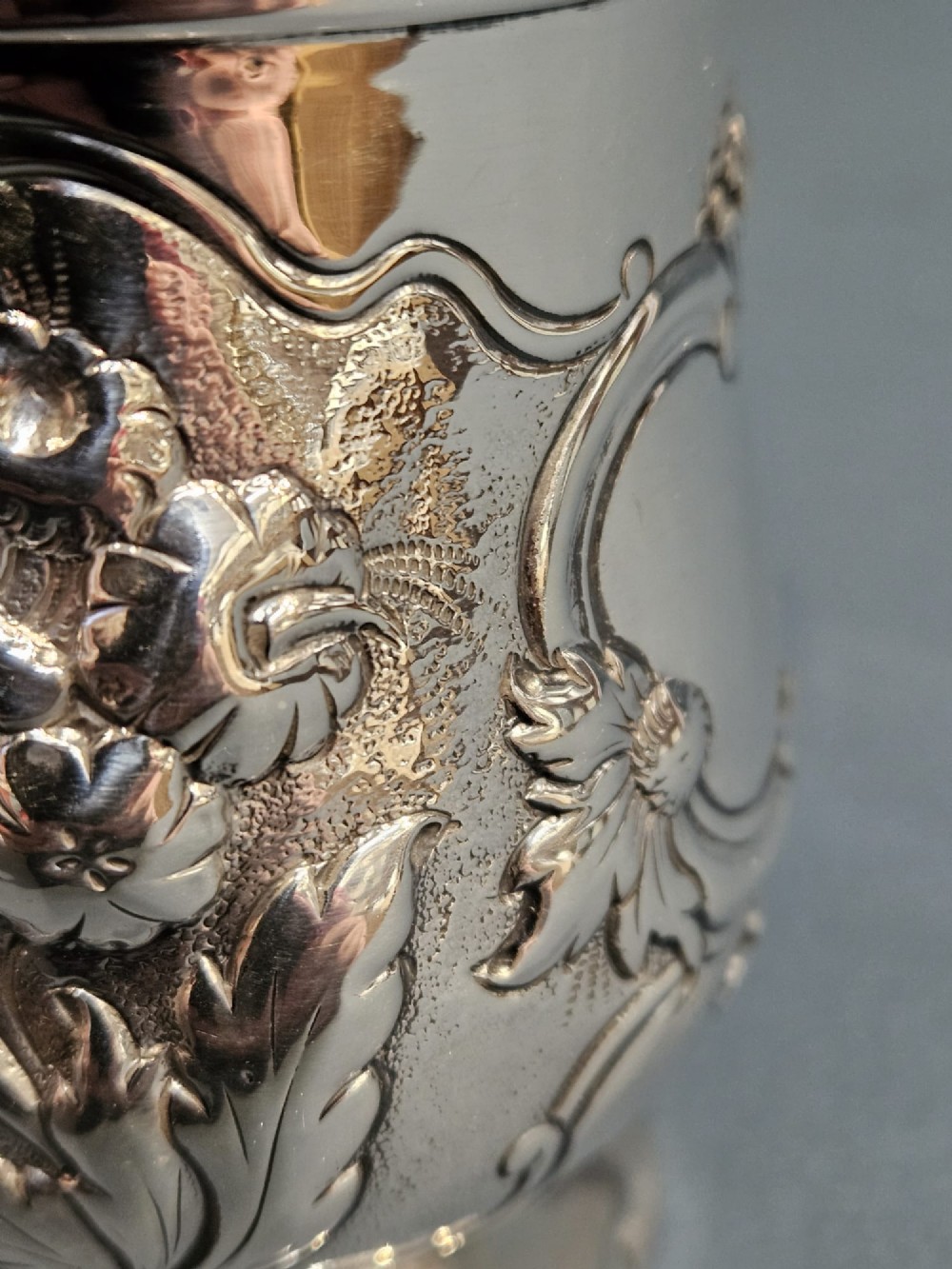 A William IV sterling silver mug featuring hand-chased floral cartouches, a scroll handle, a fluted foot, and a gilded interior. View V
