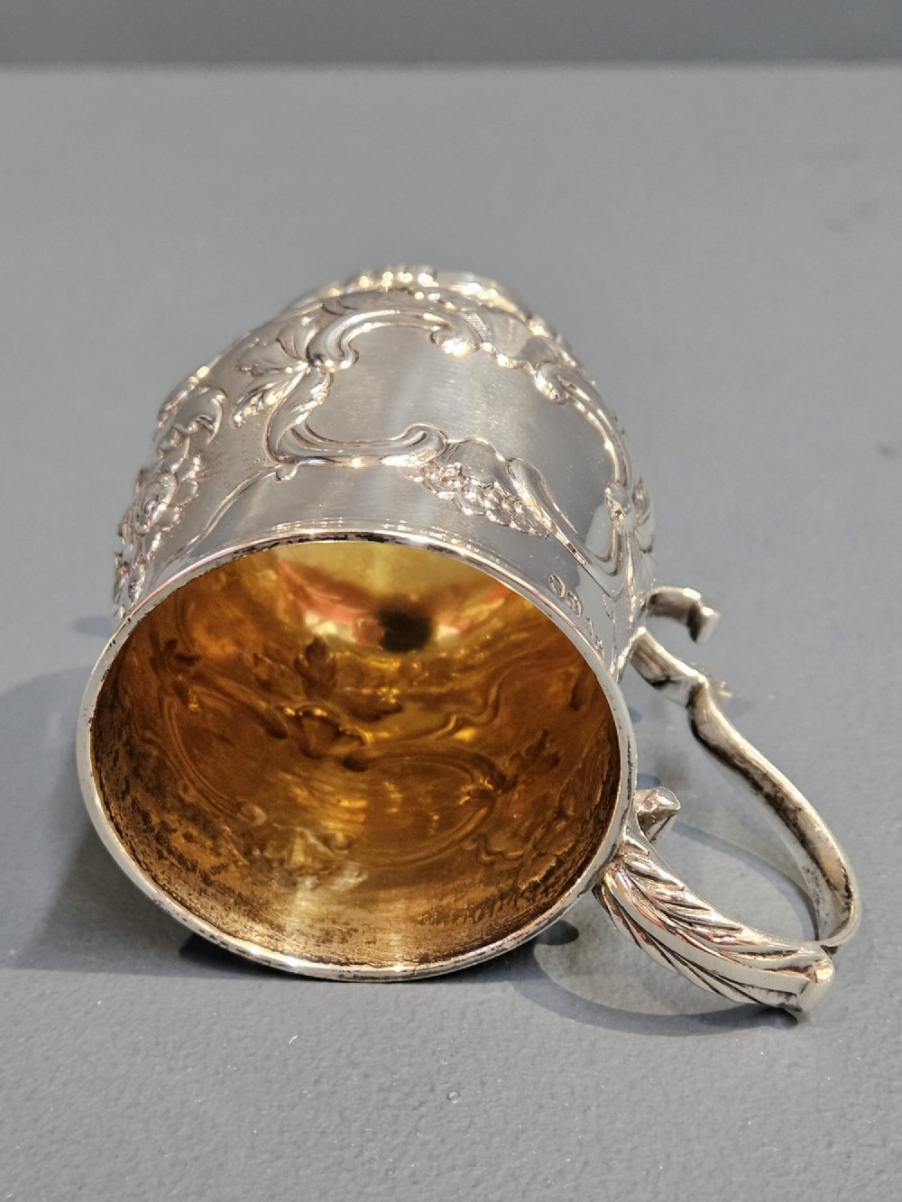 A William IV sterling silver mug featuring hand-chased floral cartouches, a scroll handle, a fluted foot, and a gilded interior. View VII