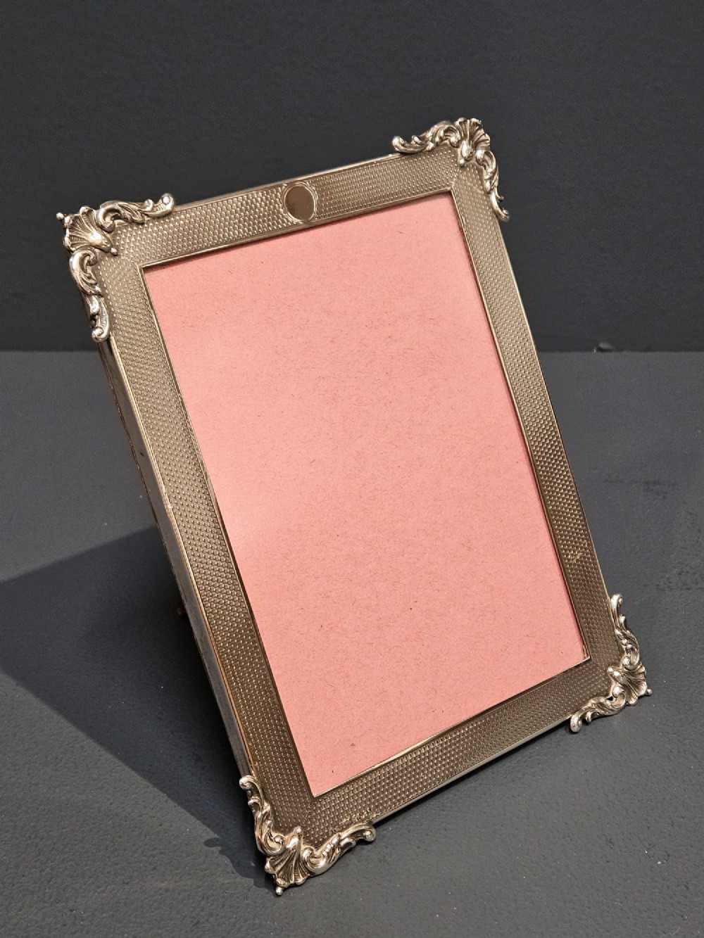 A rectangular George V sterling silver picture frame featuring engine-turned geometric engraving, ornate foliage corner mounts, and a circular top cartouche. View II