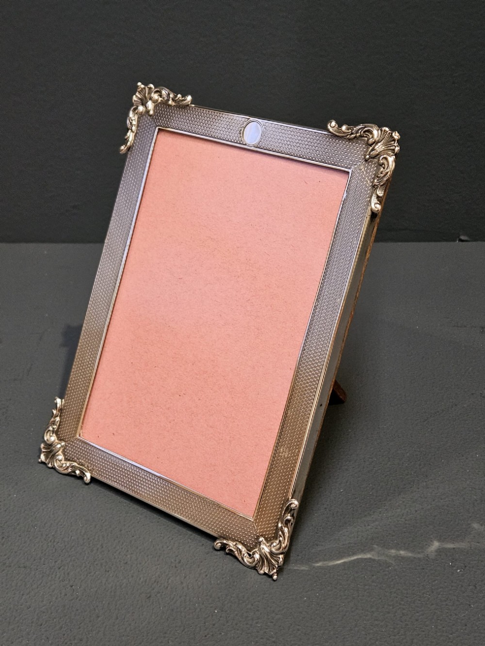 A rectangular George V sterling silver picture frame featuring engine-turned geometric engraving, ornate foliage corner mounts, and a circular top cartouche. View III