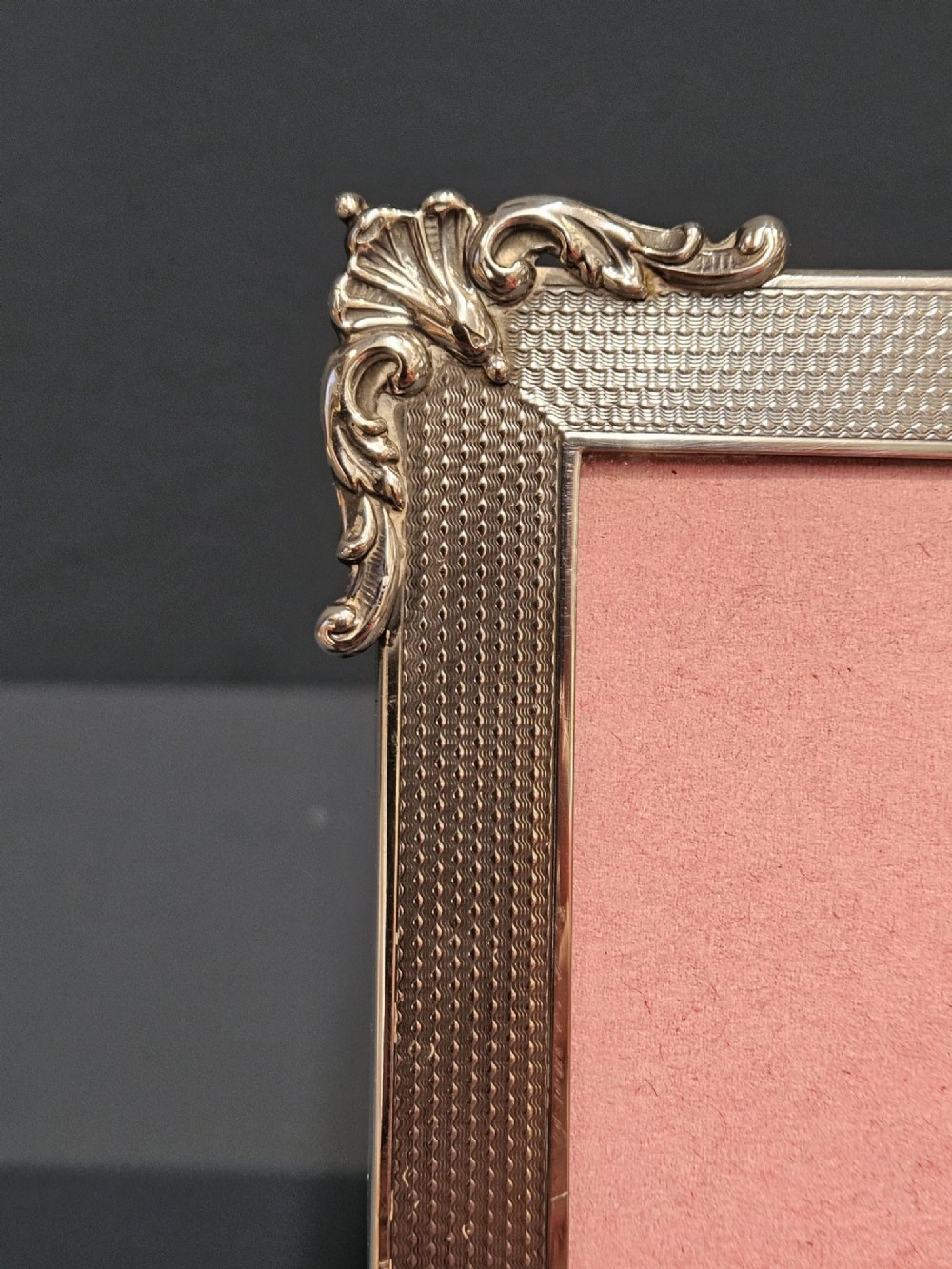 A rectangular George V sterling silver picture frame featuring engine-turned geometric engraving, ornate foliage corner mounts, and a circular top cartouche. View IV