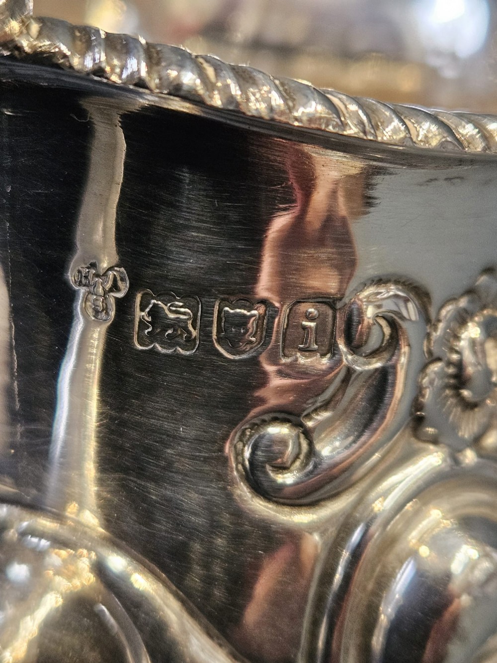 An Edwardian silver cream jug with floral embossing, a high-arched flying scroll handle, and a circular pedestal base. View VII