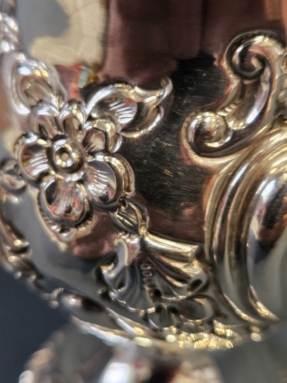 An Edwardian silver cream jug with floral embossing, a high-arched flying scroll handle, and a circular pedestal base. View VIII
