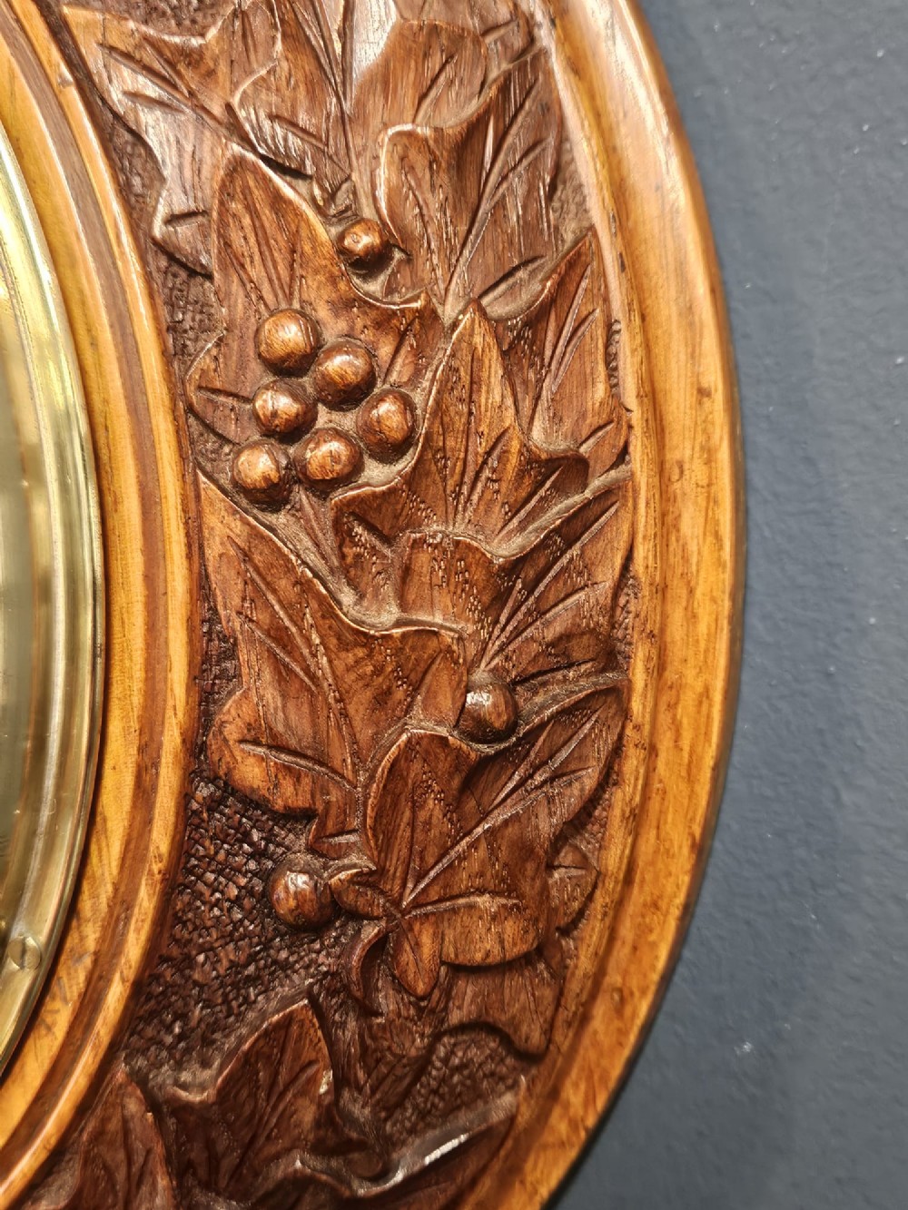 A circular Victorian aneroid barometer featuring a hand-carved oak surround with an ivy wreath pattern and a brass-rimmed silvered dial. View VI