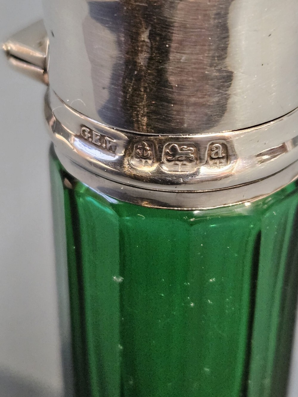 A cylindrical emerald green faceted glass scent bottle featuring a smooth silver cap stamped with hallmarks. View II