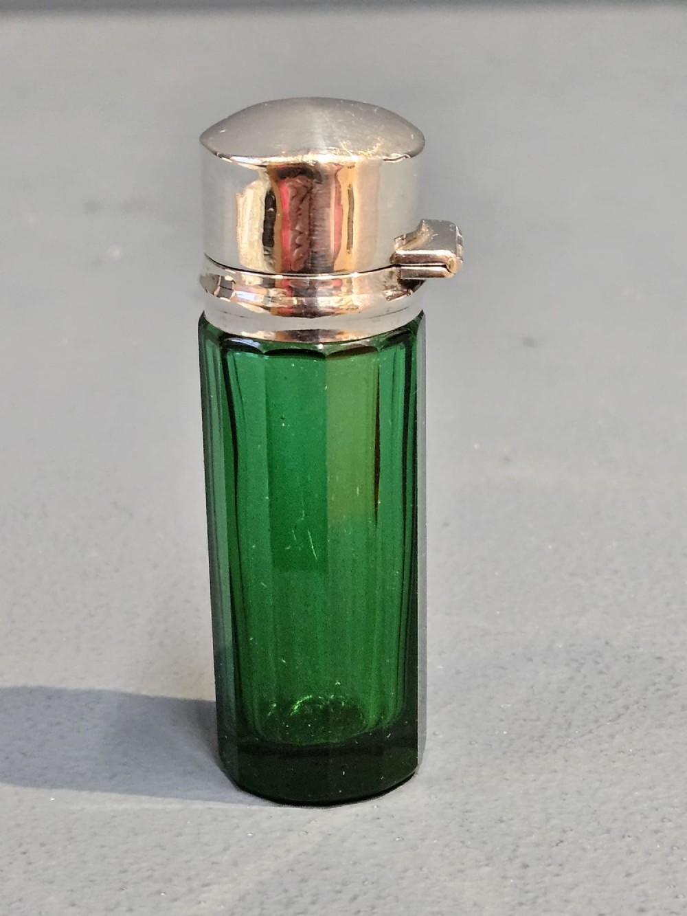 A cylindrical emerald green faceted glass scent bottle featuring a smooth silver cap stamped with hallmarks. View III