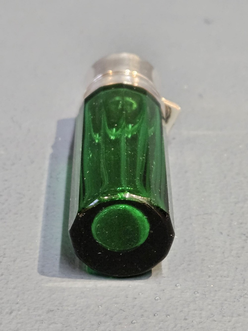 A cylindrical emerald green faceted glass scent bottle featuring a smooth silver cap stamped with hallmarks. View IV
