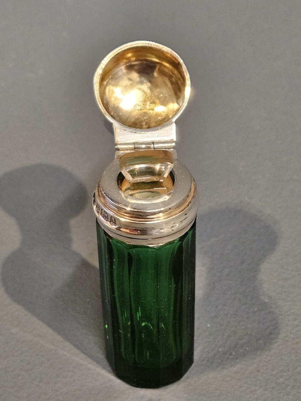 A cylindrical emerald green faceted glass scent bottle featuring a smooth silver cap stamped with hallmarks. View V