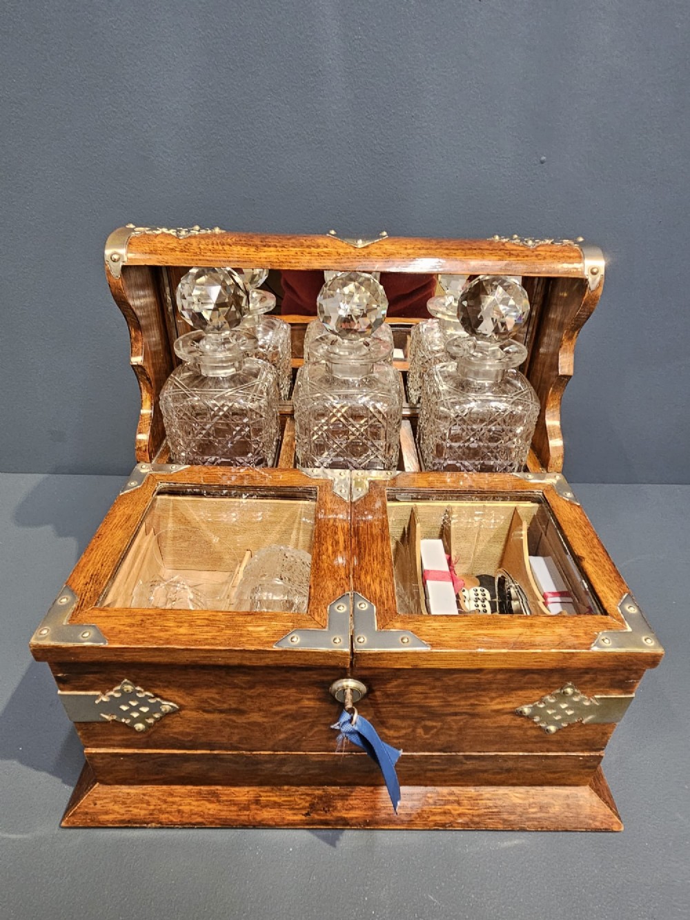 A Victorian oak tantalus featuring brass corner mounts, three cut-glass decanters with faceted stoppers set against a mirrored back, and forward-folding compartments for gaming accessories. View III