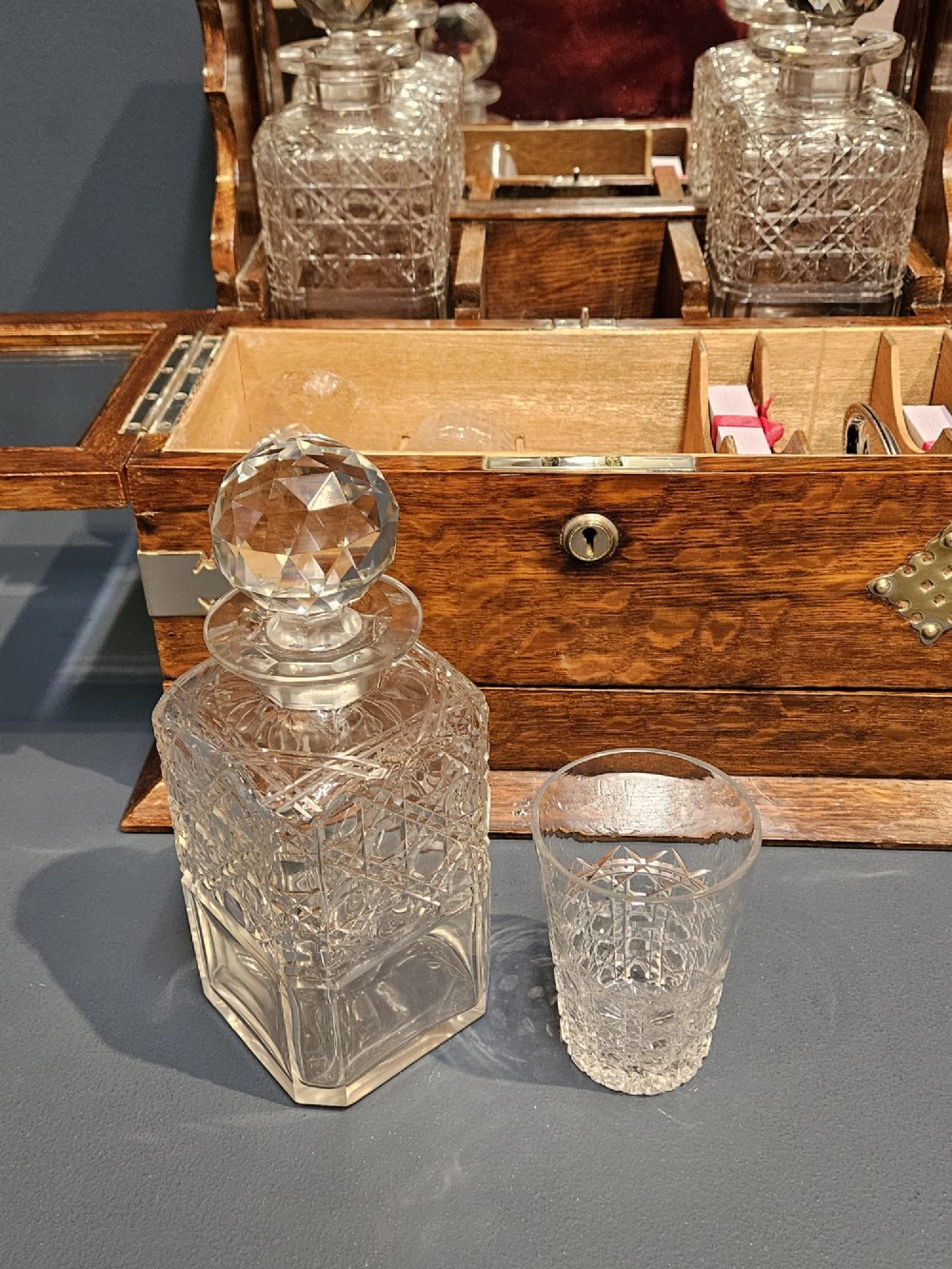 A Victorian oak tantalus featuring brass corner mounts, three cut-glass decanters with faceted stoppers set against a mirrored back, and forward-folding compartments for gaming accessories. View VII