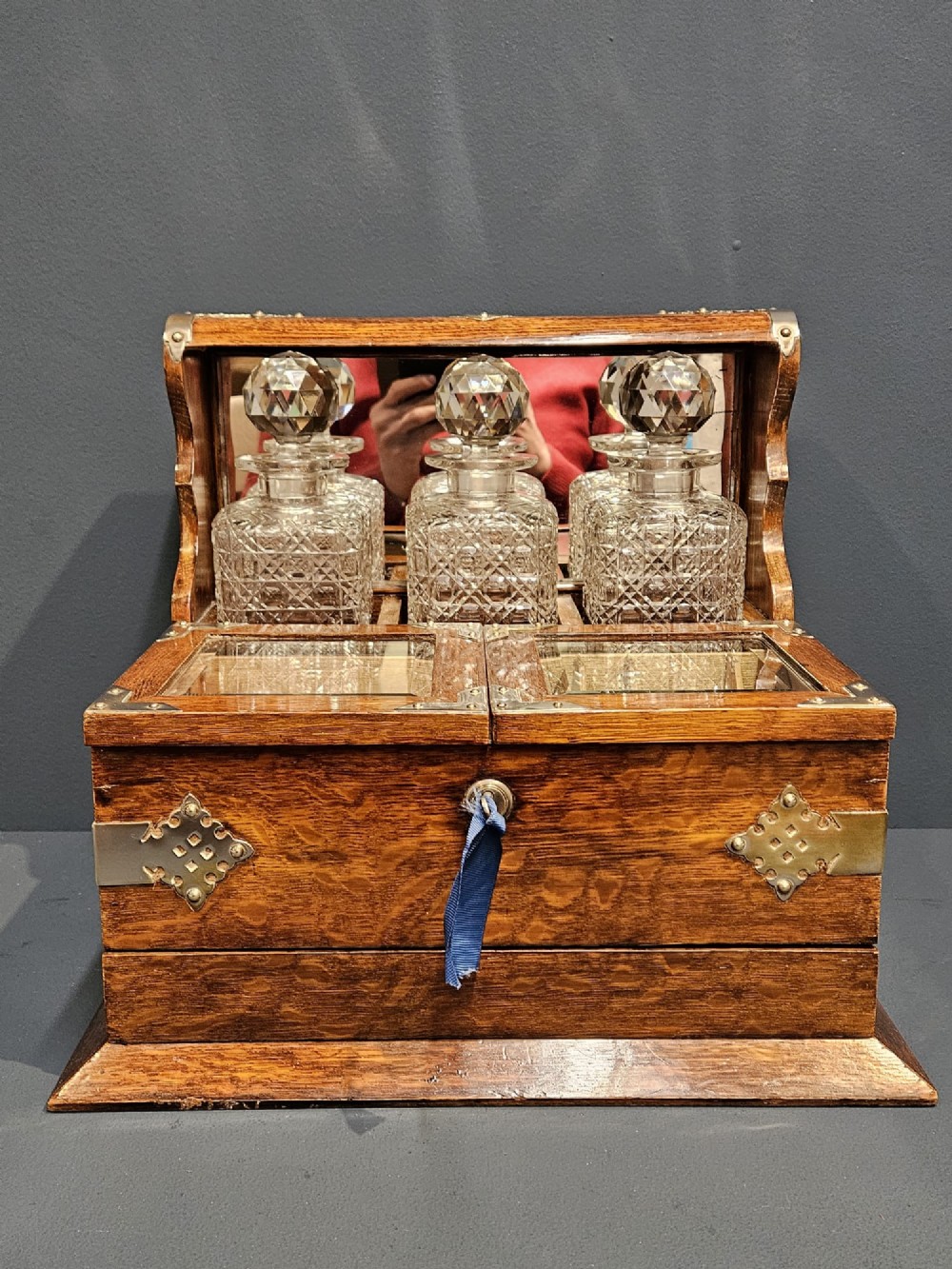 A Victorian oak tantalus featuring brass corner mounts, three cut-glass decanters with faceted stoppers set against a mirrored back, and forward-folding compartments for gaming accessories. View VIII