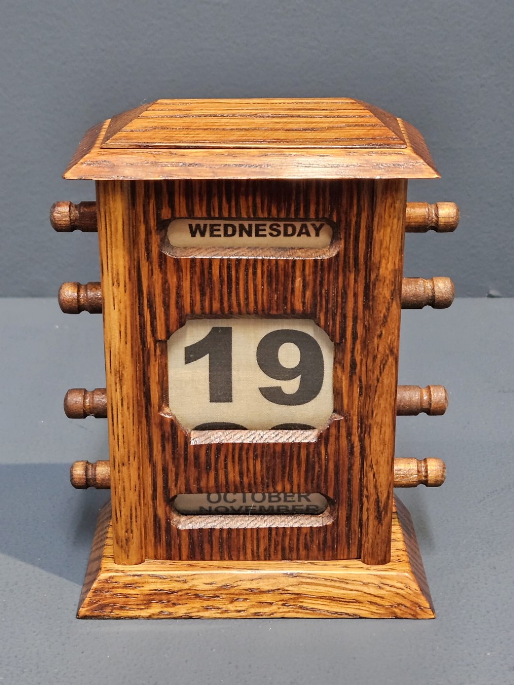 An Edwardian oak perpetual desk calendar featuring four side adjustment knobs, a moulded top, and cut-out apertures displaying the day, date, and month. View IV