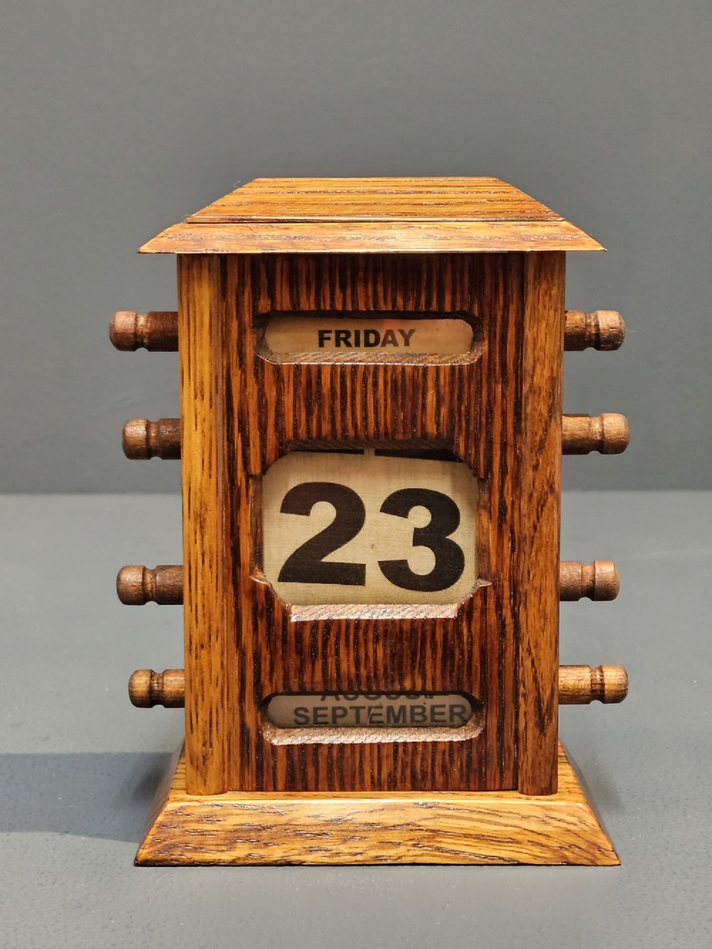 An Edwardian oak perpetual desk calendar featuring four side adjustment knobs, a moulded top, and cut-out apertures displaying the day, date, and month. View V