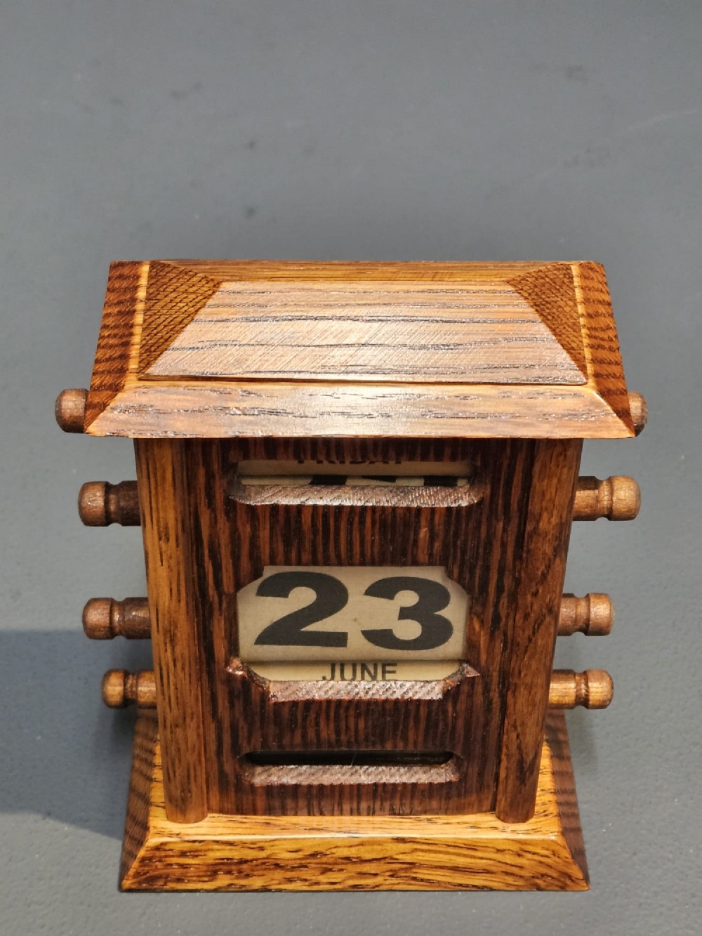 An Edwardian oak perpetual desk calendar featuring four side adjustment knobs, a moulded top, and cut-out apertures displaying the day, date, and month. View VI