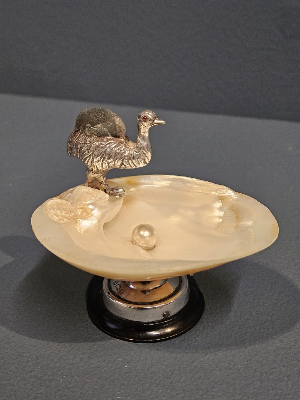 An Edwardian sterling silver emu figurine with an embedded fabric pin cushion, mounted on a polished mother-of-pearl shell dish.