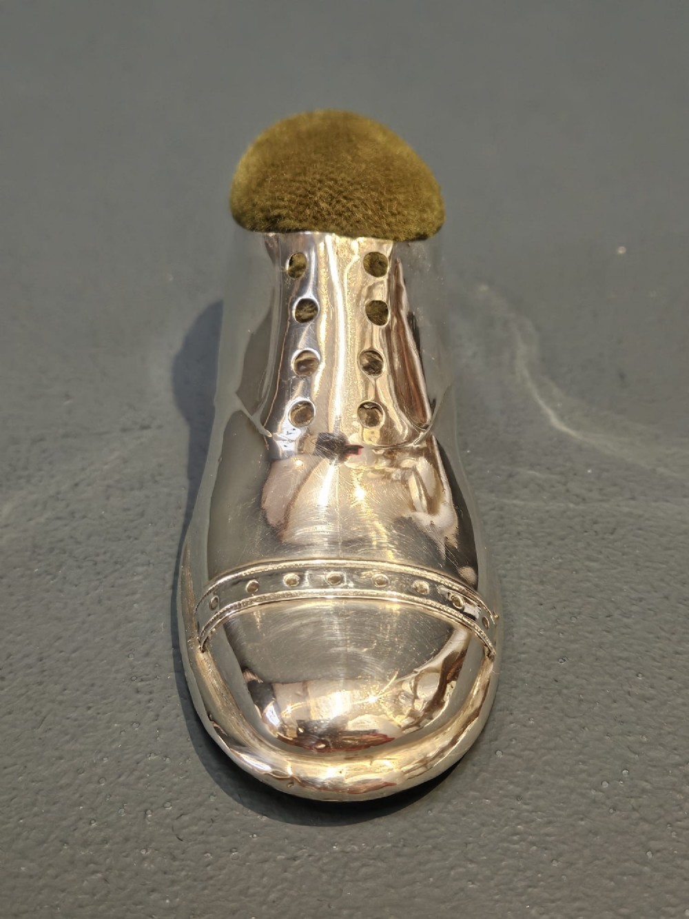 An Edwardian hallmarked sterling silver pin cushion shaped like a gentlemans shoe with an olive green velvet cushion top. View V
