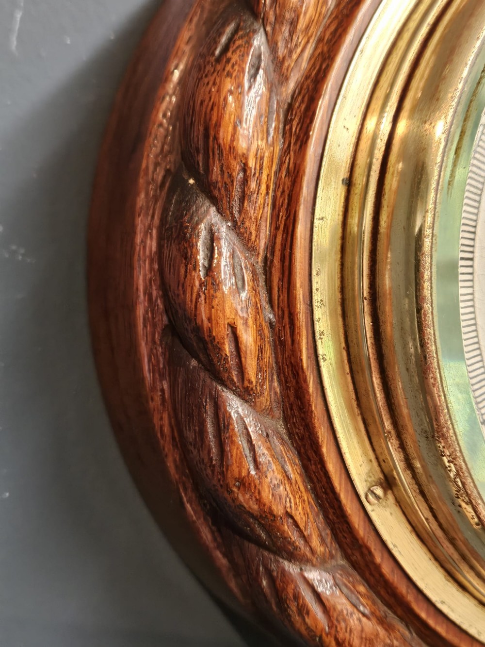 A circular antique oak aneroid barometer featuring a carved rope twist border, brass bezel, and detailed ceramic dial with black lettering. View IV
