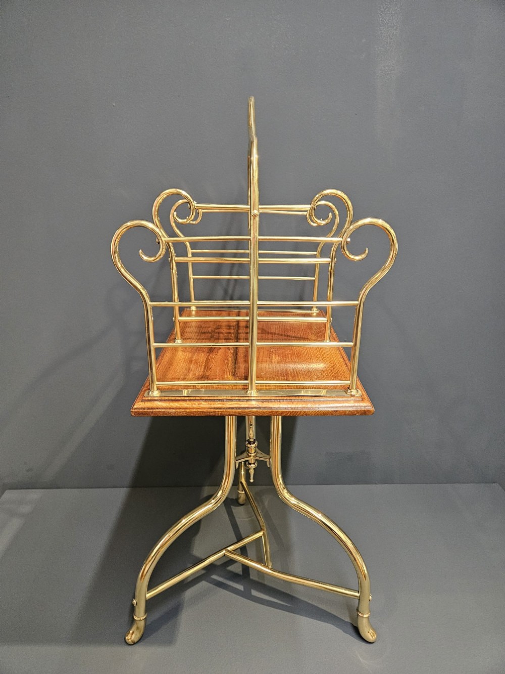 A Victorian revolving book stand featuring a polished brass wire rack mounted on a square oak surface supported by a brass tripod base.