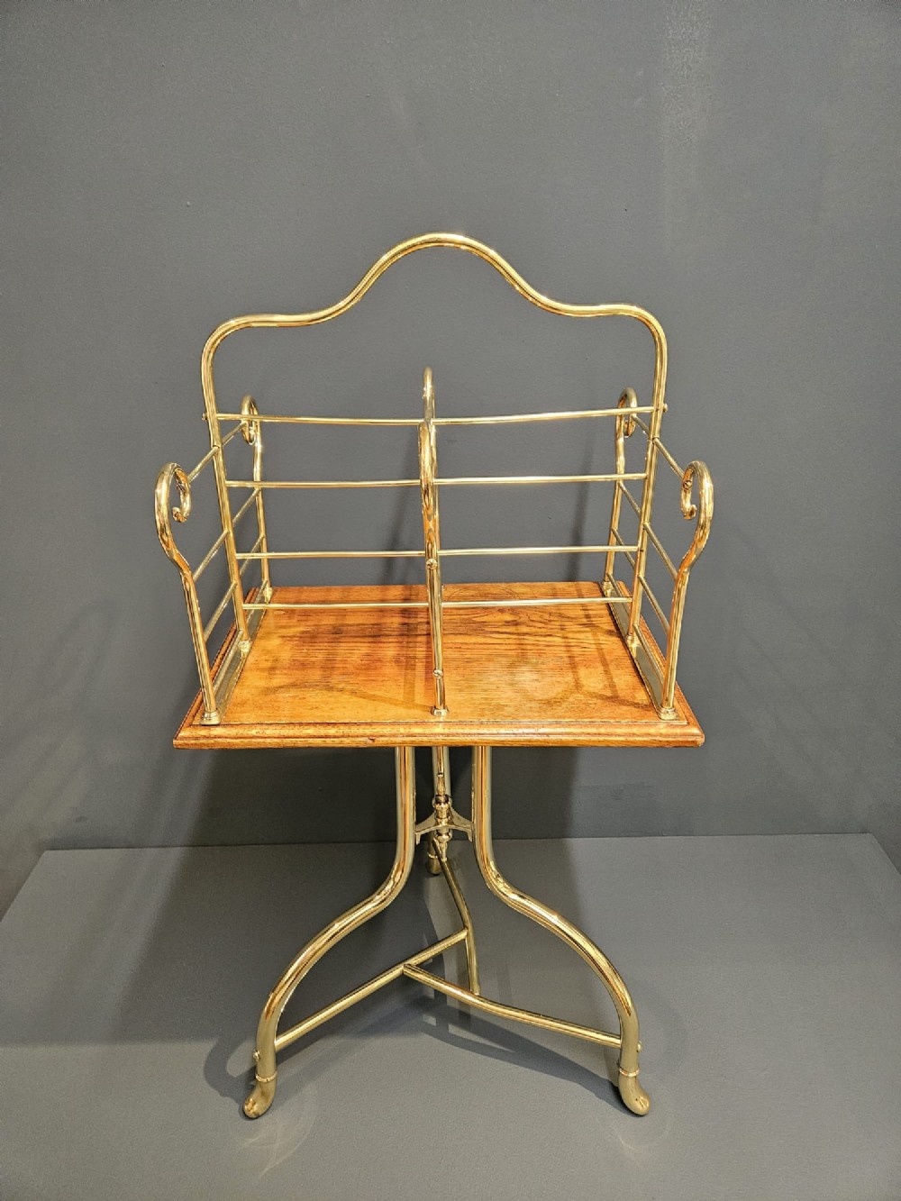 A Victorian revolving book stand featuring a polished brass wire rack mounted on a square oak surface supported by a brass tripod base. View II