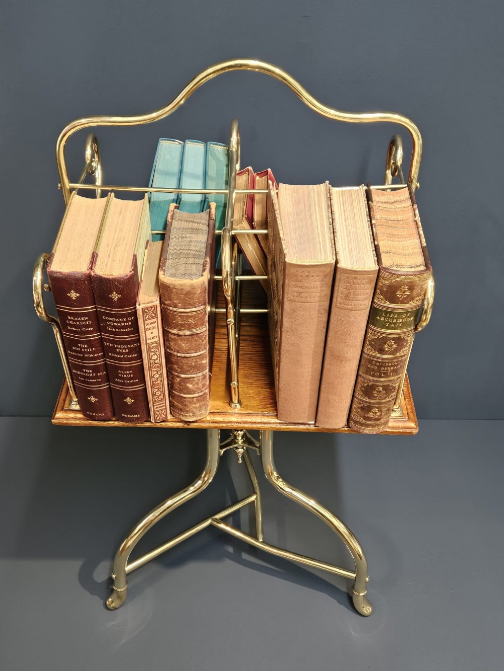 A Victorian revolving book stand featuring a polished brass wire rack mounted on a square oak surface supported by a brass tripod base. View III