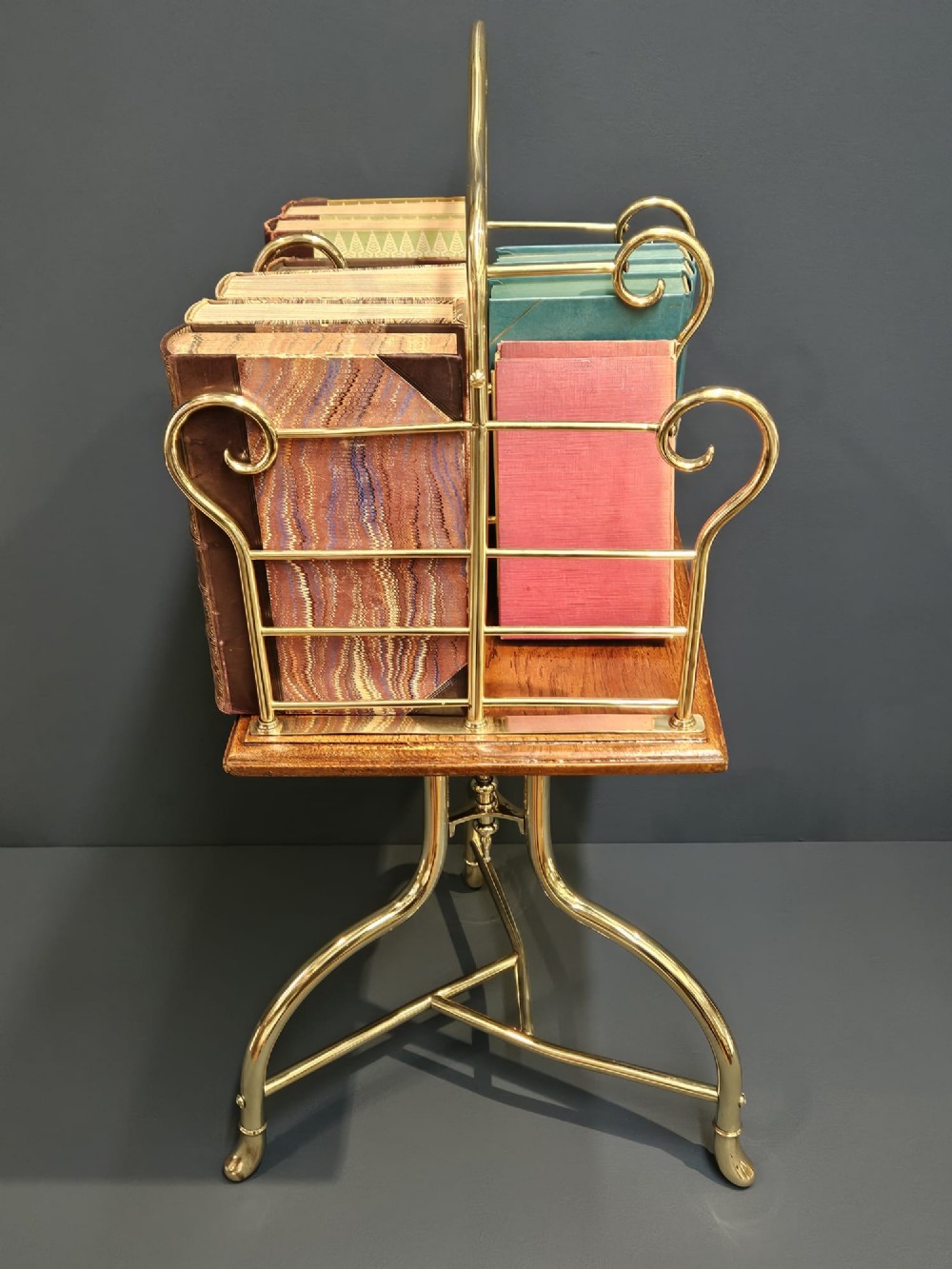 A Victorian revolving book stand featuring a polished brass wire rack mounted on a square oak surface supported by a brass tripod base. View IV