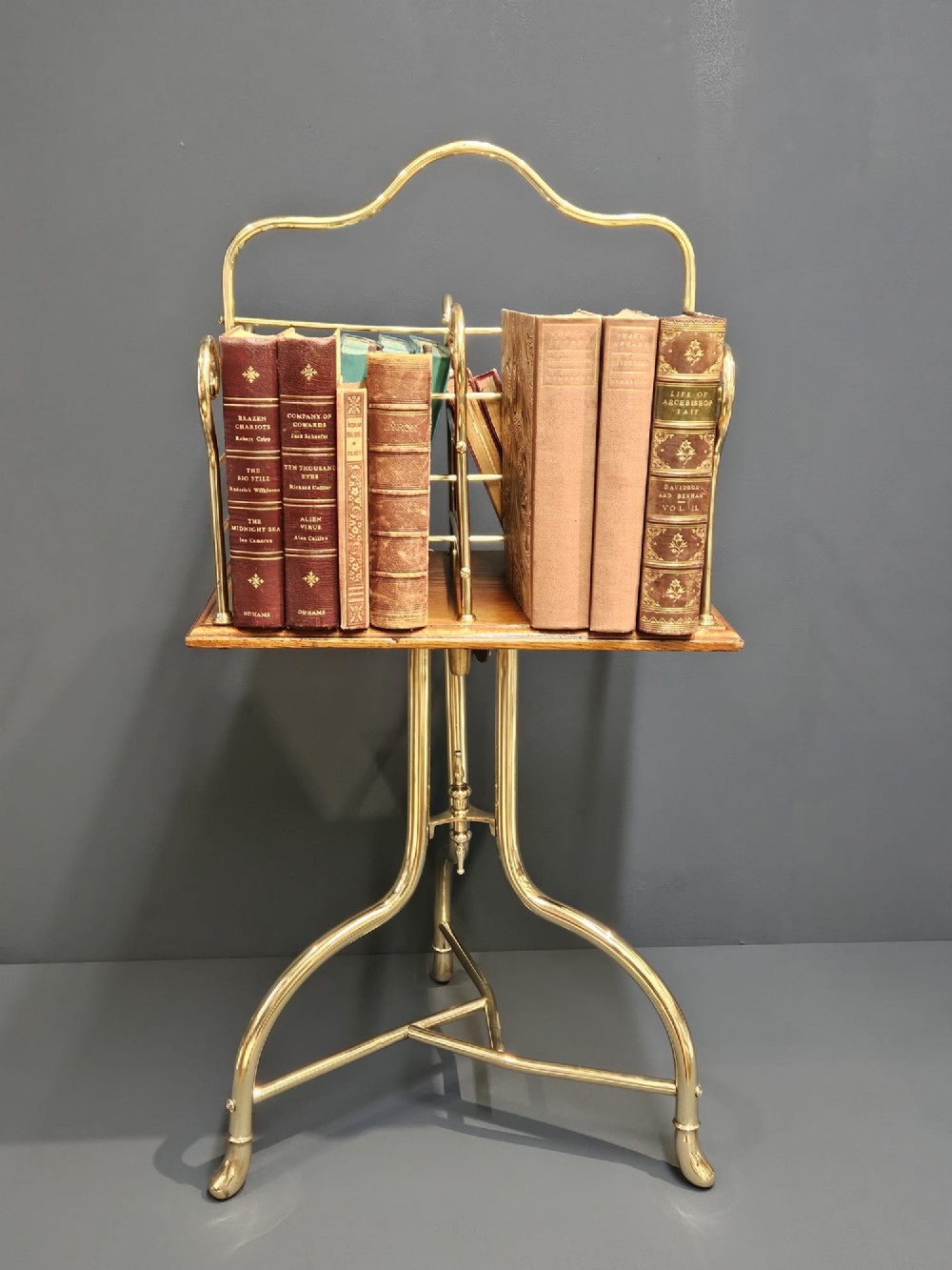 A Victorian revolving book stand featuring a polished brass wire rack mounted on a square oak surface supported by a brass tripod base. View VI
