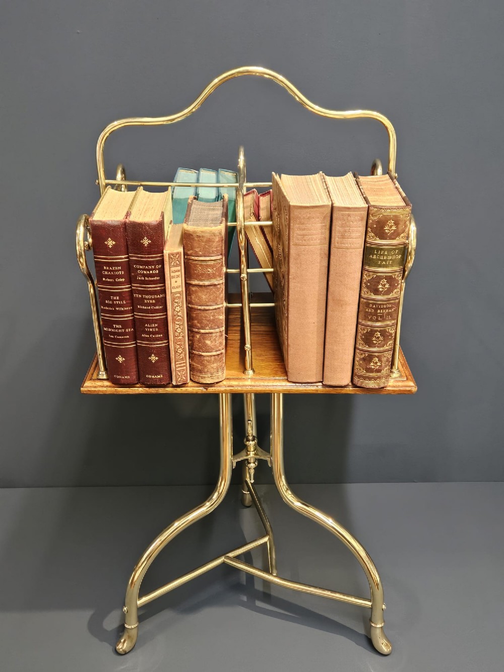 A Victorian revolving book stand featuring a polished brass wire rack mounted on a square oak surface supported by a brass tripod base. View VII