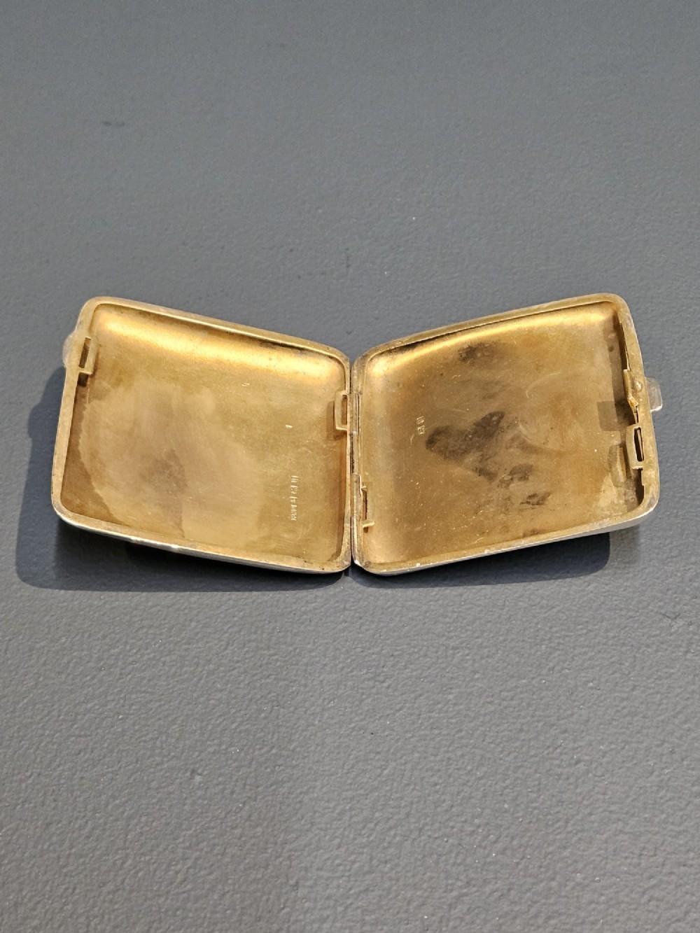 A square metallic silver pocket case featuring detailed chased foliate scrollwork and a central blank cartouche. View VI