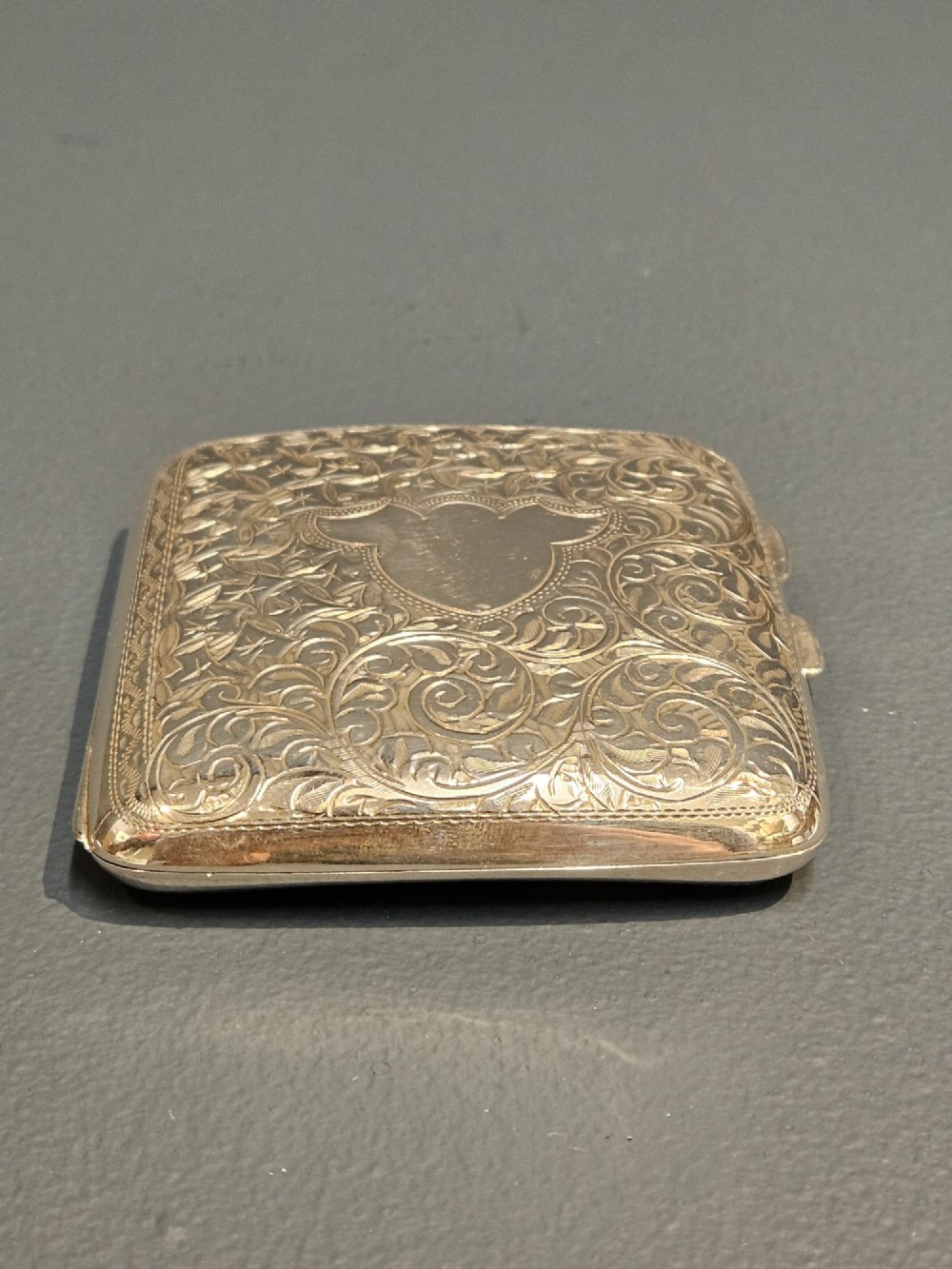 A square metallic silver pocket case featuring detailed chased foliate scrollwork and a central blank cartouche. View VII