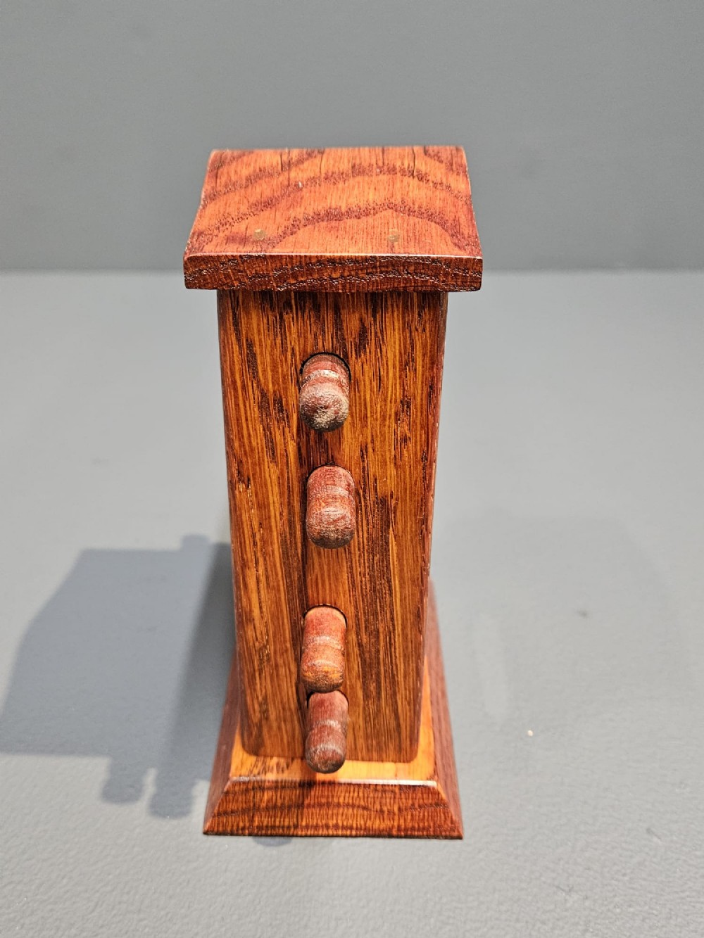 An Edwardian carved oak perpetual desk calendar featuring side turning pegs and printed linen date scrolls behind rectangular window openings. View IV
