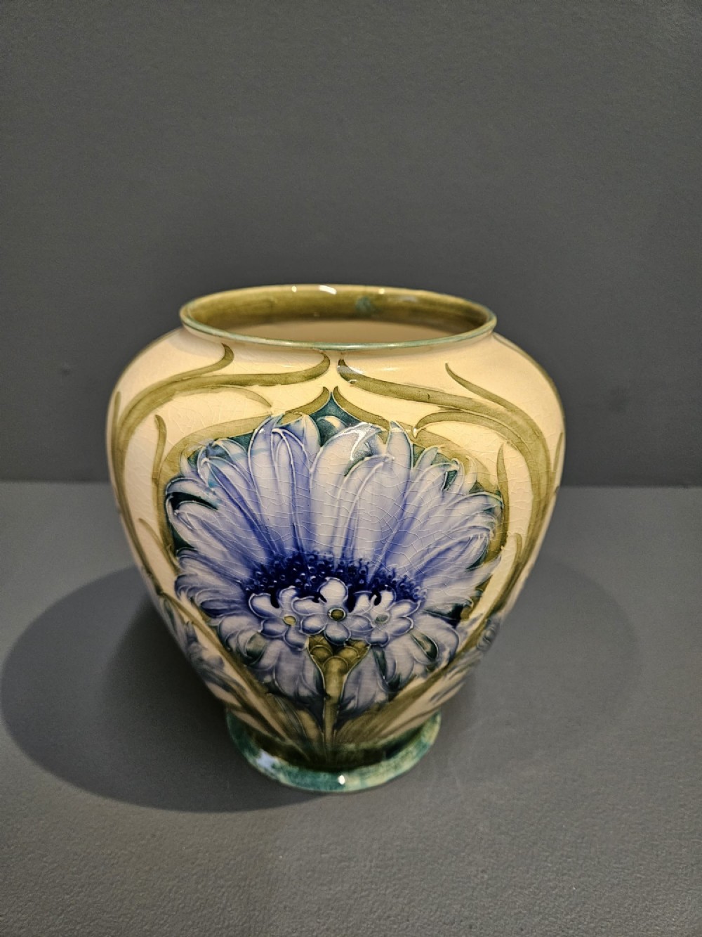 A bulbous ceramic vase featuring tube-lined blue cornflower motifs with green foliage set against a cream background.