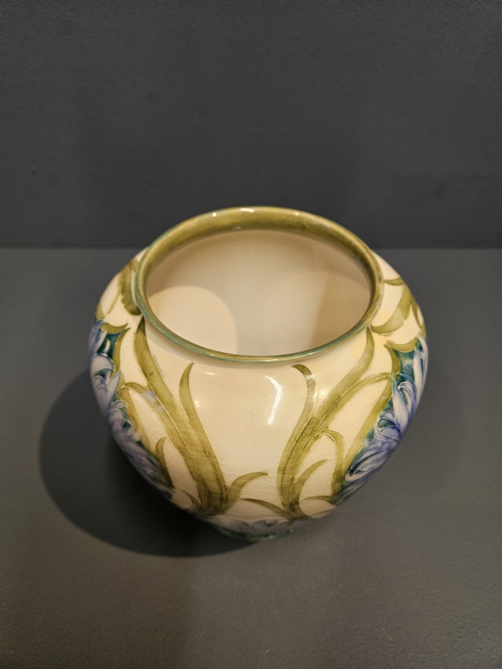 A bulbous ceramic vase featuring tube-lined blue cornflower motifs with green foliage set against a cream background. View II