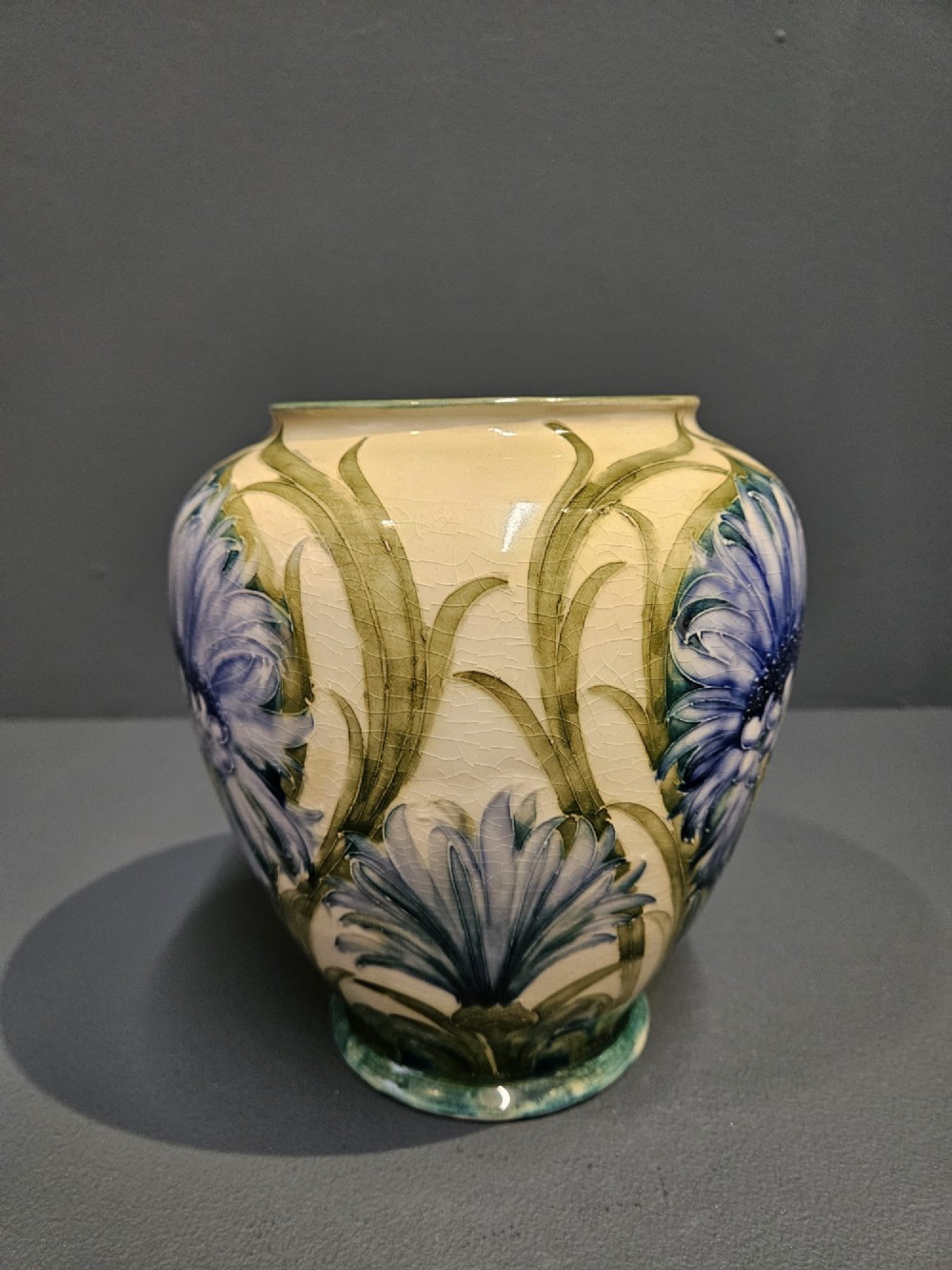 A bulbous ceramic vase featuring tube-lined blue cornflower motifs with green foliage set against a cream background. View IV
