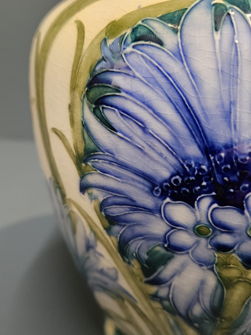 A bulbous ceramic vase featuring tube-lined blue cornflower motifs with green foliage set against a cream background. View V