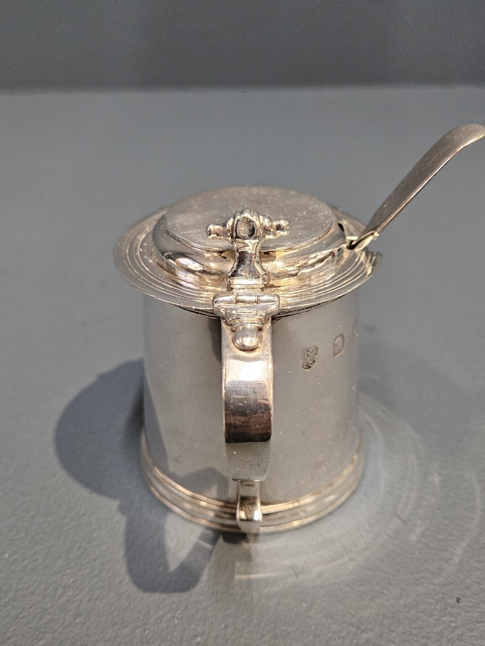 A cylindrical Britannia silver mustard pot featuring a scalloped collar rim, stepped lid with shell finial, and an inserted silver spoon. View III