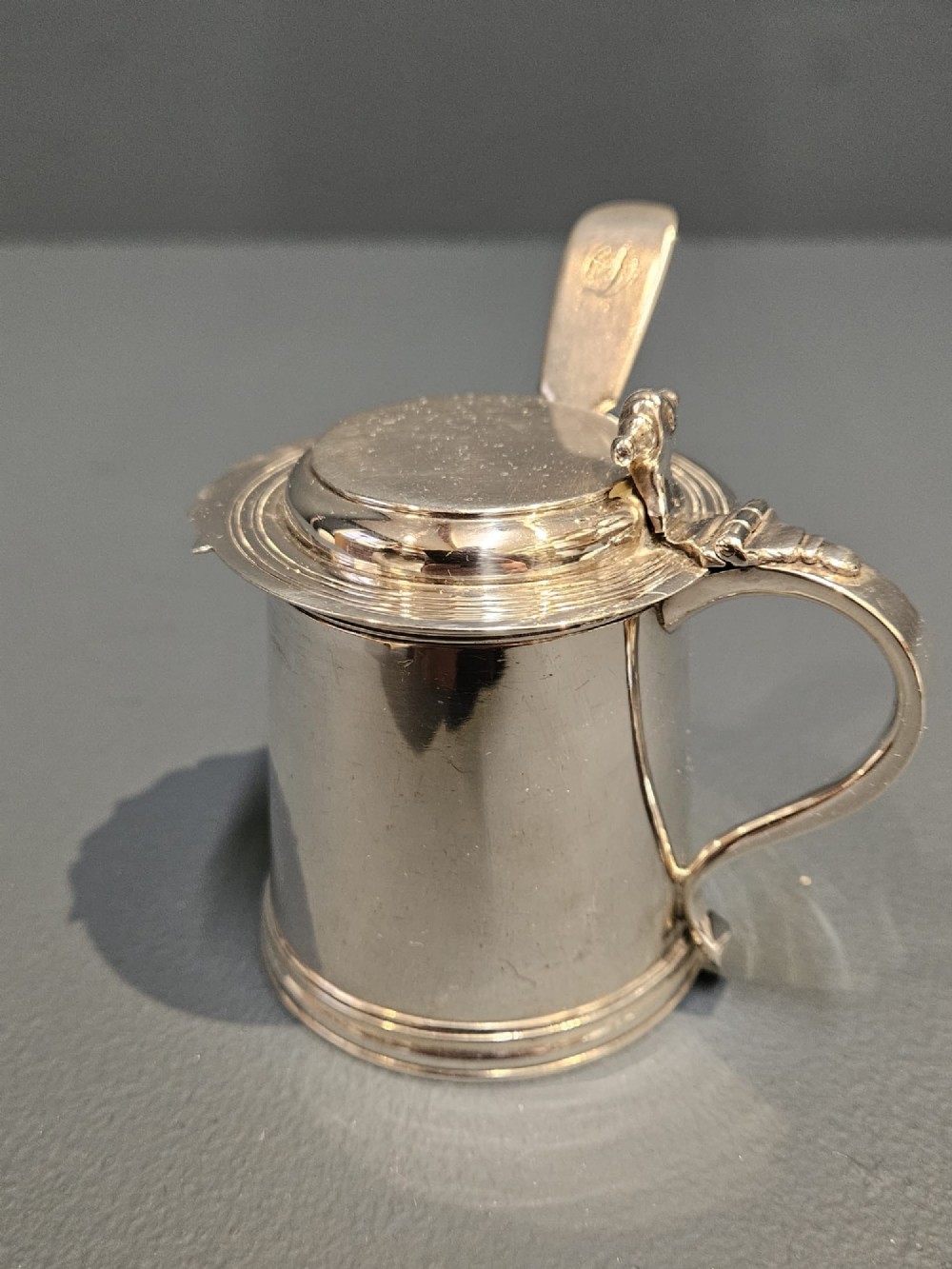 A cylindrical Britannia silver mustard pot featuring a scalloped collar rim, stepped lid with shell finial, and an inserted silver spoon. View IV