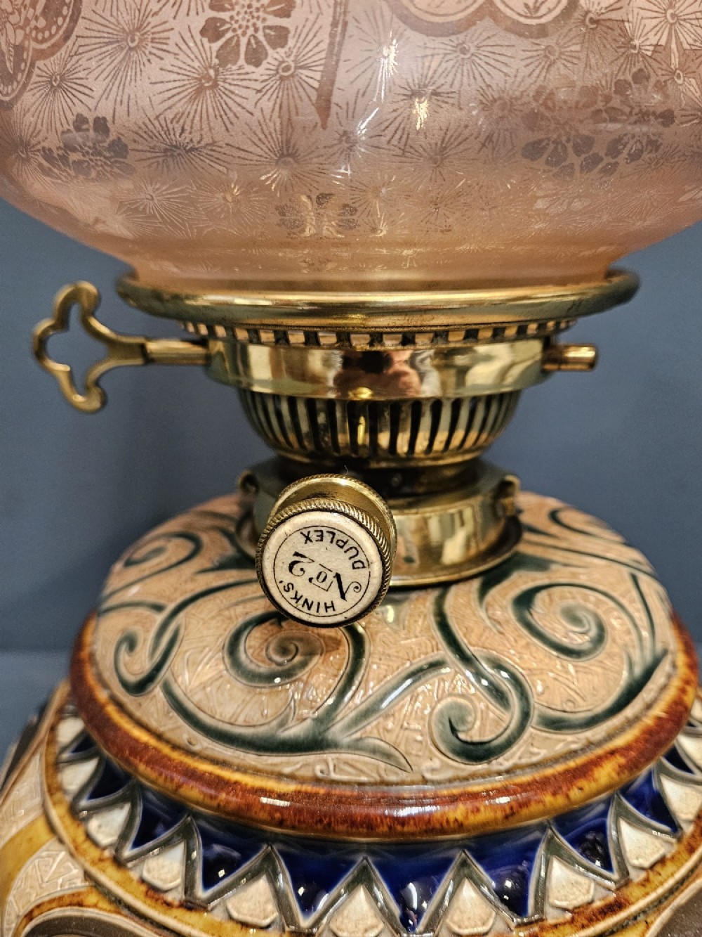 A Victorian Doulton Lambeth stoneware oil lamp featuring an incised ceramic base on claw feet, a brass burner, a glass chimney, and a frilled pink etched shade. View II