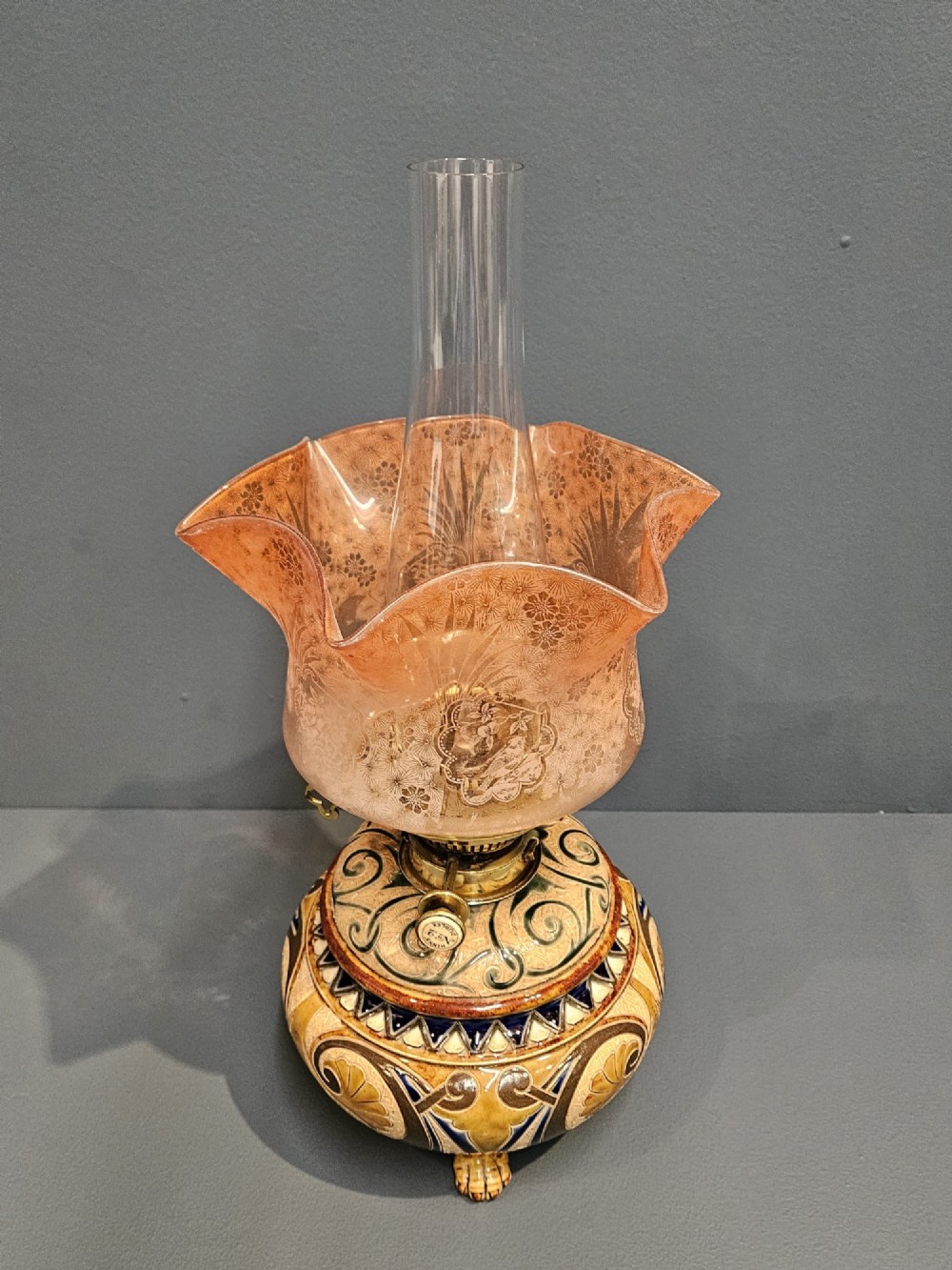 A Victorian Doulton Lambeth stoneware oil lamp featuring an incised ceramic base on claw feet, a brass burner, a glass chimney, and a frilled pink etched shade. View IV