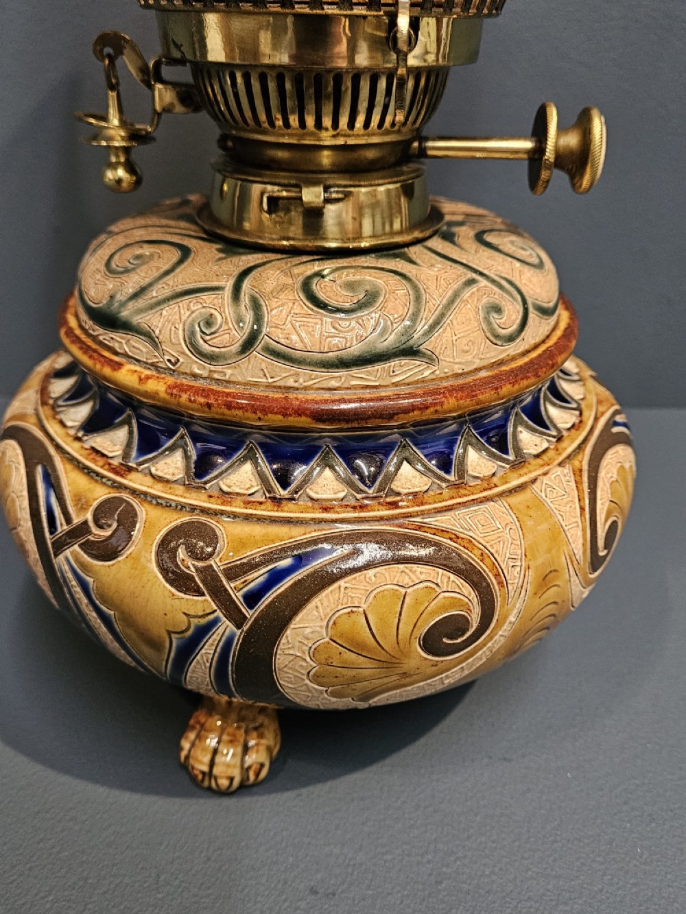 A Victorian Doulton Lambeth stoneware oil lamp featuring an incised ceramic base on claw feet, a brass burner, a glass chimney, and a frilled pink etched shade. View VII