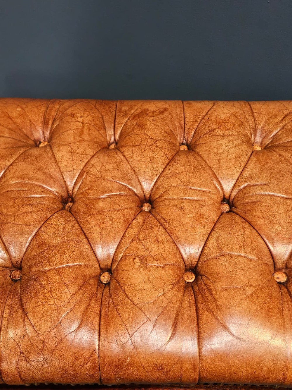 A rectangular 1930s footstool featuring deep-buttoned tan leather upholstery, brass studding along the perimeter, and square timber legs with stretchers. View III
