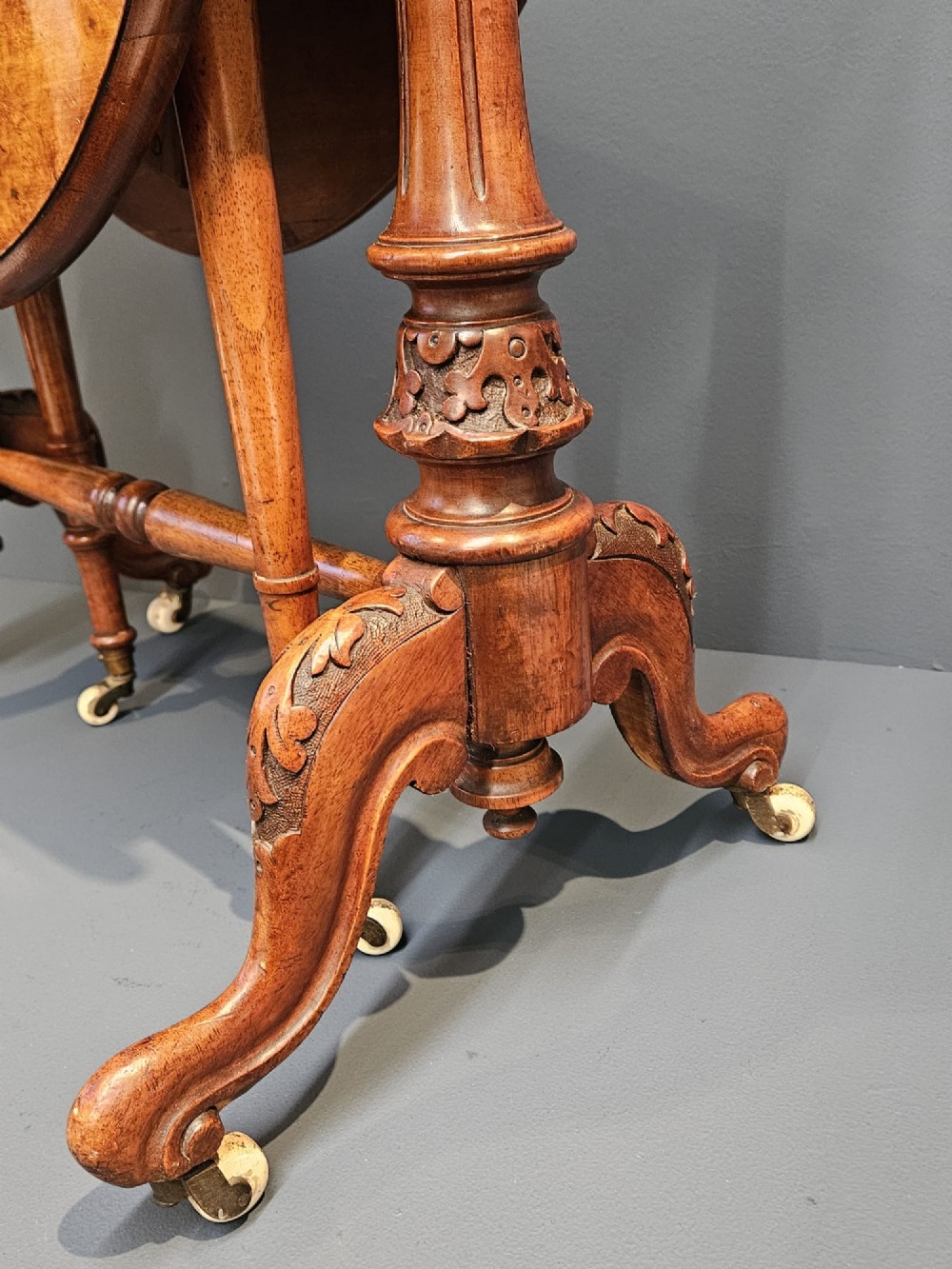 A Victorian burr walnut baby Sutherland table featuring two drop leaves, dual turned column supports, and carved feet on white ceramic castors. View II