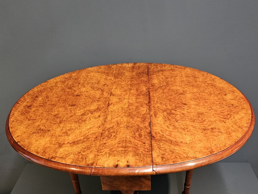 A Victorian burr walnut baby Sutherland table featuring two drop leaves, dual turned column supports, and carved feet on white ceramic castors. View VI