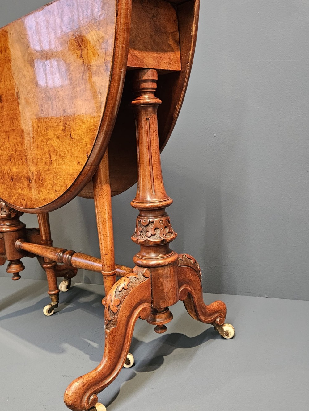 A Victorian burr walnut baby Sutherland table featuring two drop leaves, dual turned column supports, and carved feet on white ceramic castors. View VII